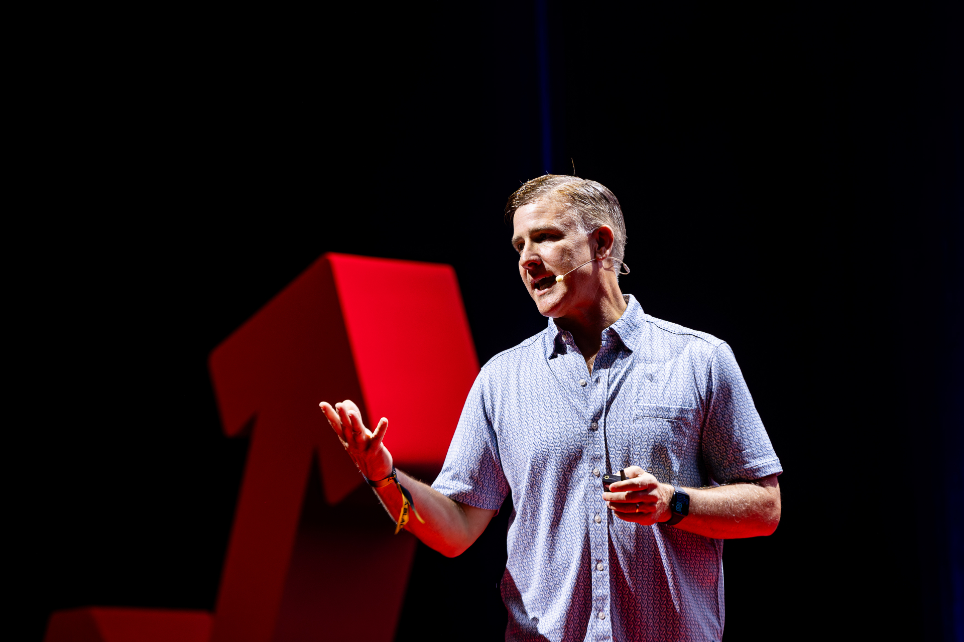 Sean Ellis speaking on stage with a red geometric shape in the background
